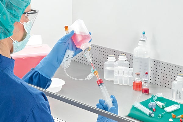 Lab personnel wearing protective clothing preparing medication inside a laminar air flow cabinet (LAF).